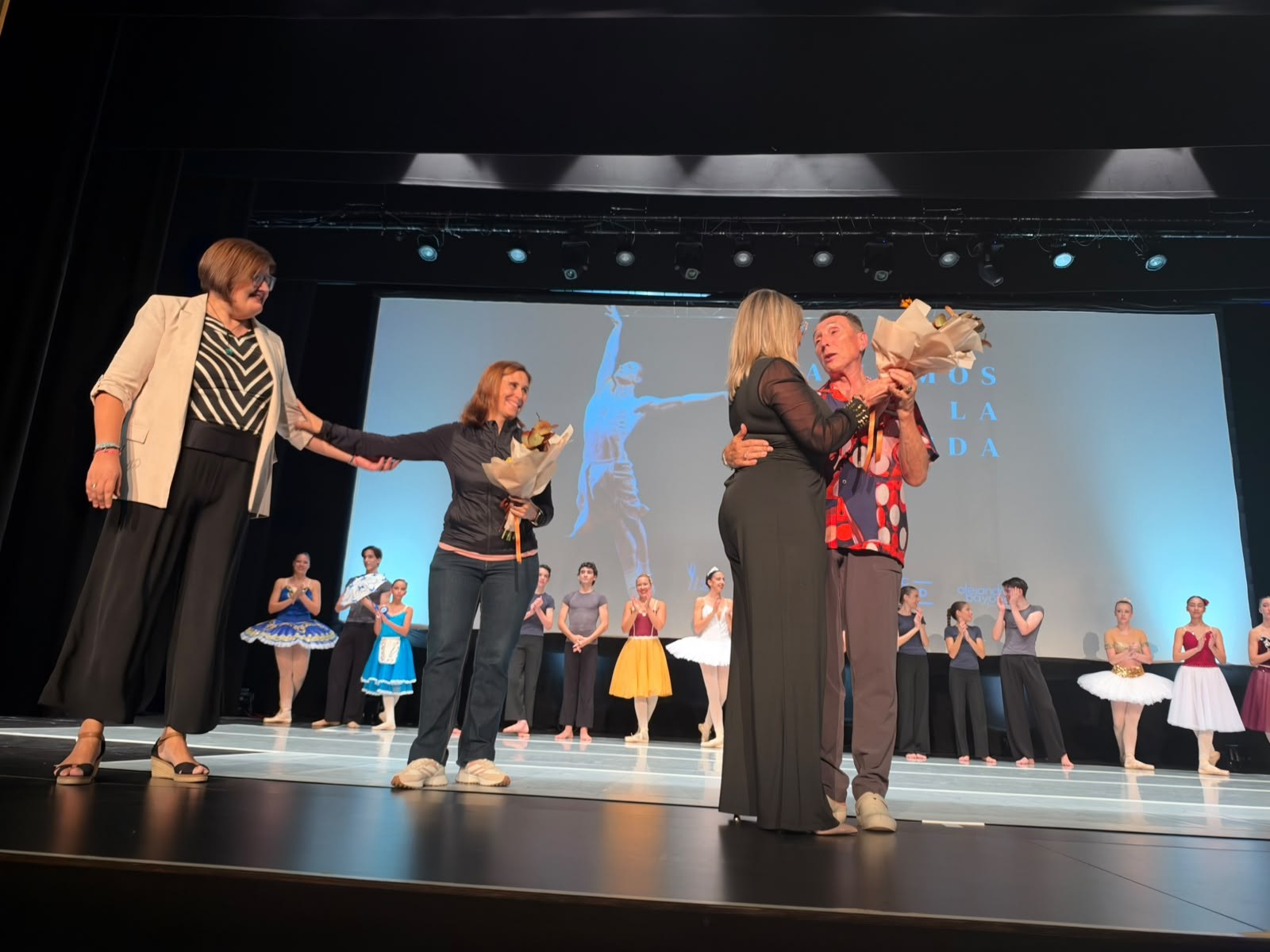 Momento de agradecimiento en el escenario de Bailemos por la vida con bailarinas al fondo.